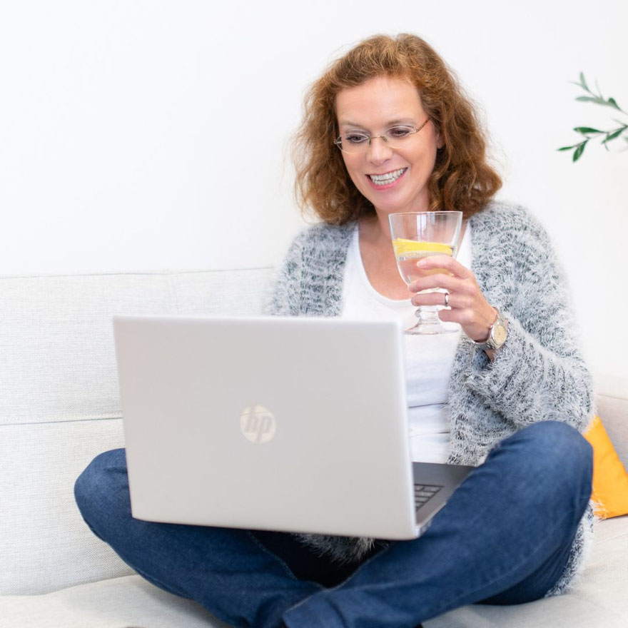 Frau mit Brille am Laptop mit Wasserglas in grauer Strickjacke