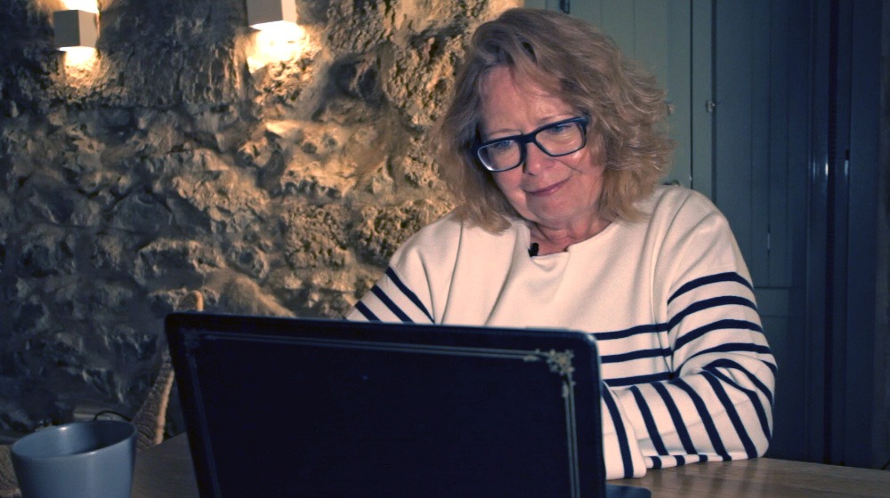 Vera am Laptop arbeitet vor steinerner Wand lächelnd