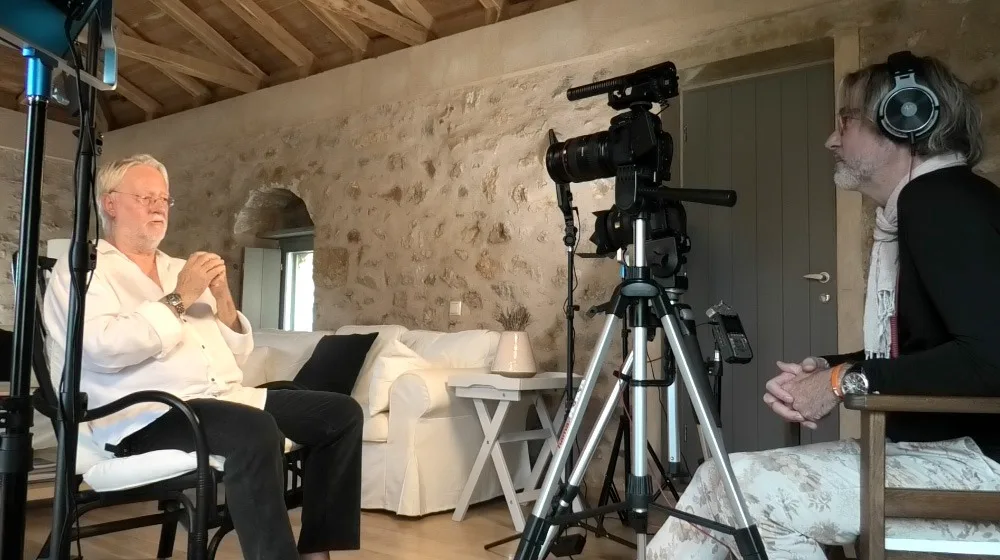 Älterer Mann in weißem Hemd sitzt vor Kamera und Beleuchtung im Studio