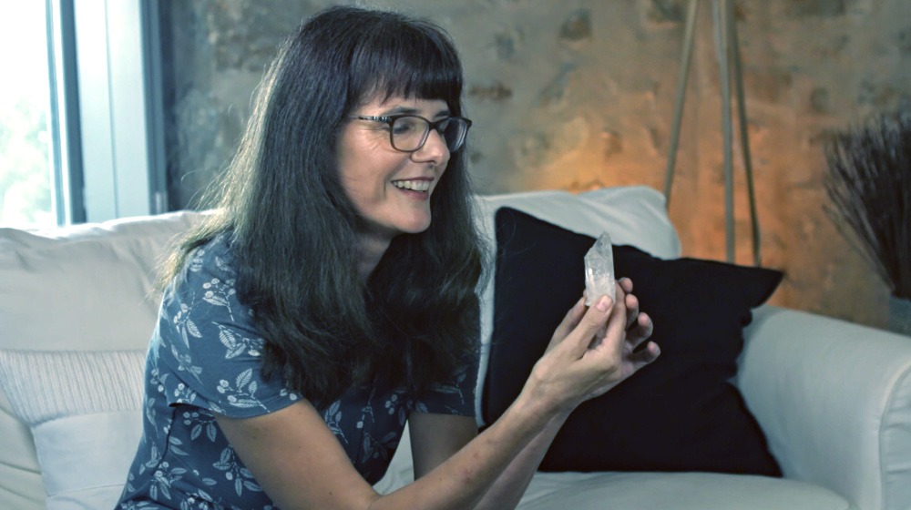 Catalina mit Brille und Blumenmuster-Shirt sitzt lachend auf Couch