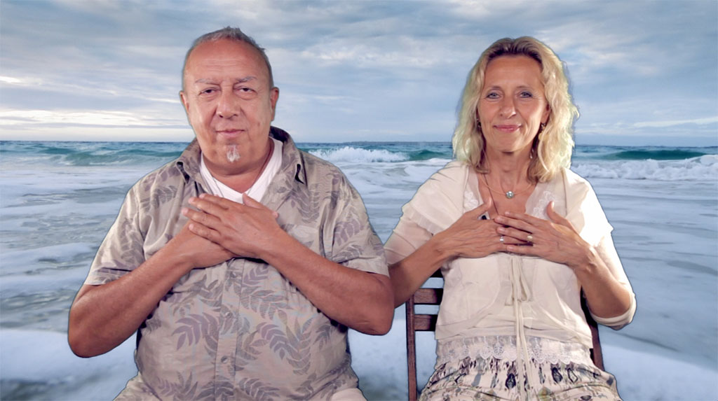 Mann und Frau mit Händen auf der Brust am Strand vor Meer und Himmel