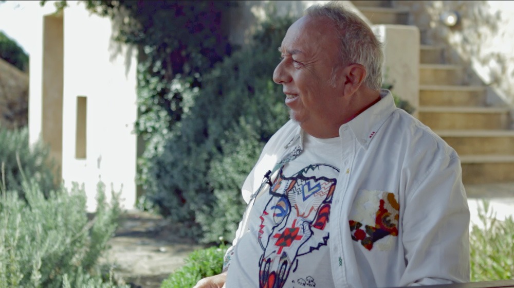 Mann (Taato) auf Freitreppen mit Efeu, weißes Shirt mit Muster, lächelnd