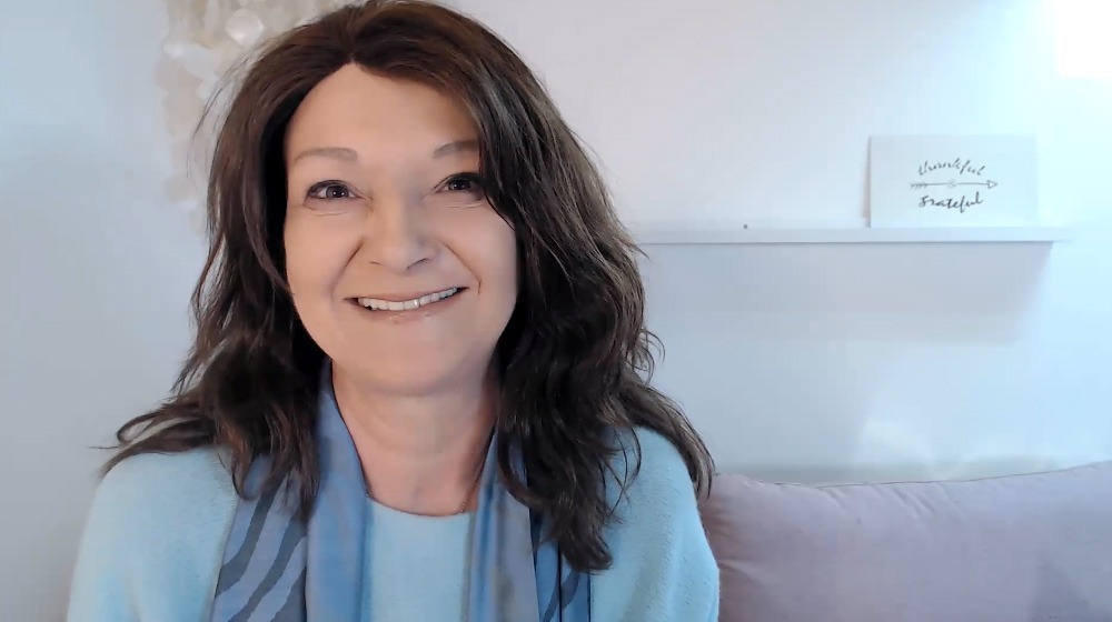 Frau Anke mit dunklen Haaren lächelt in die Kamera vor hellem Hintergrund