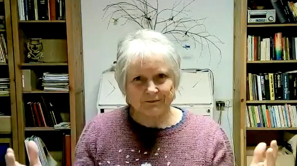 Ältere Frau Christa mit weißem Haar vor Bücherregal, spricht in Kamera