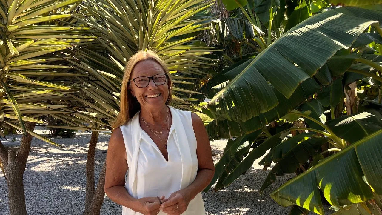 Frau mit Brille lächelt strahlend zwischen tropischen Palmen