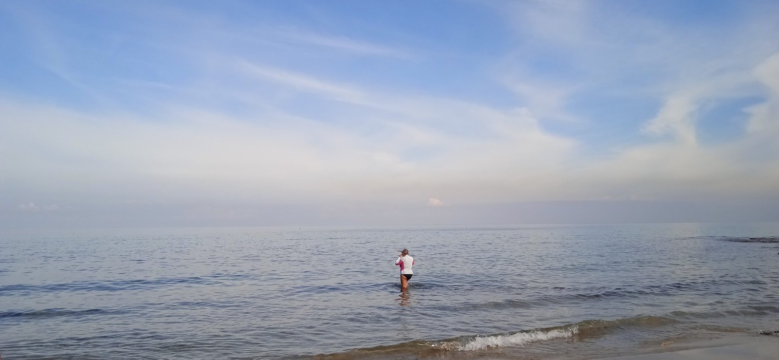 Frau joggt am Strand ins Meer mit ruhiger Wasseroberfläche und klarem Himmel
