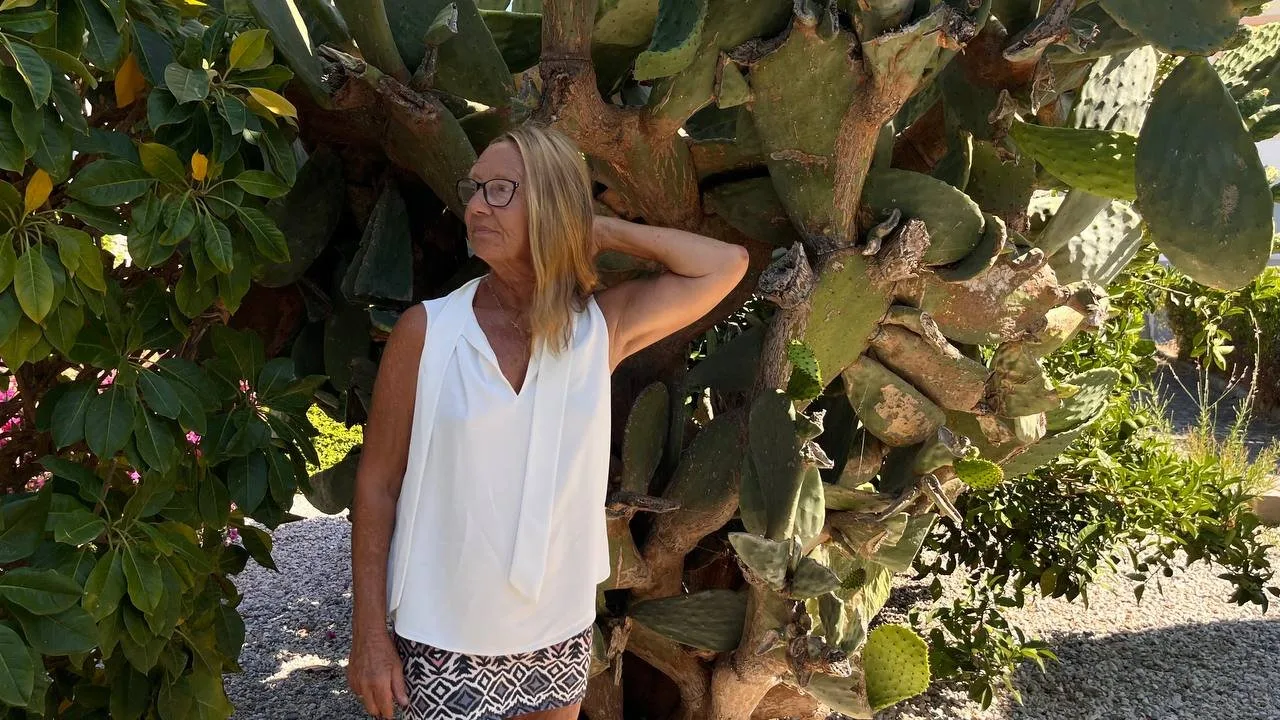 Frau mit Brille in weißem Top neben Kaktus mit Hand in Hüfte