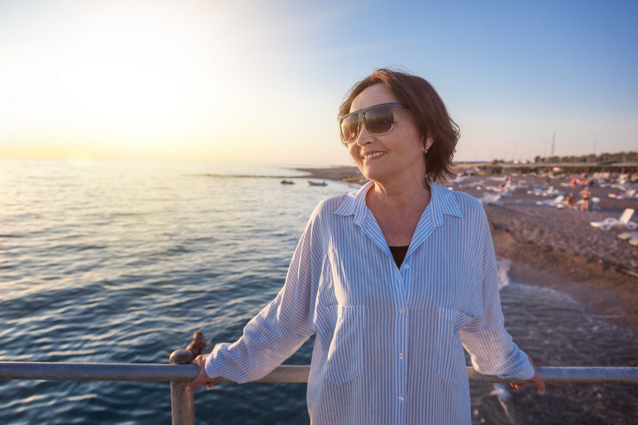 Frau mit Sonnenbrille am Pier mit Meerblick und Strand im Hintergrund