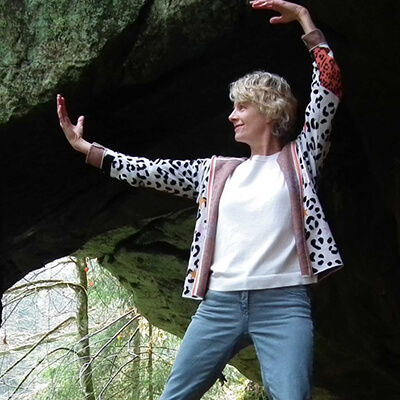Porträt von Angela Krueger, ältere Frau mit blondem Haar mit Armen nach oben vor Felsenhintergrund