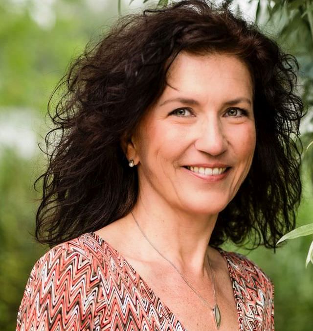 Frau Christiane Elsinger mit lockigen dunklen Haaren, rosa-gemustertem Oberteil, Porträt vor grünem Hintergrund