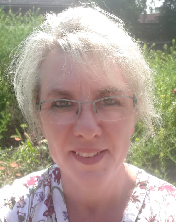 Frau Elke Bühring mit weißem Haar, Brille, rosa Ton, Porträt vor grünem Garten-Hintergrund
