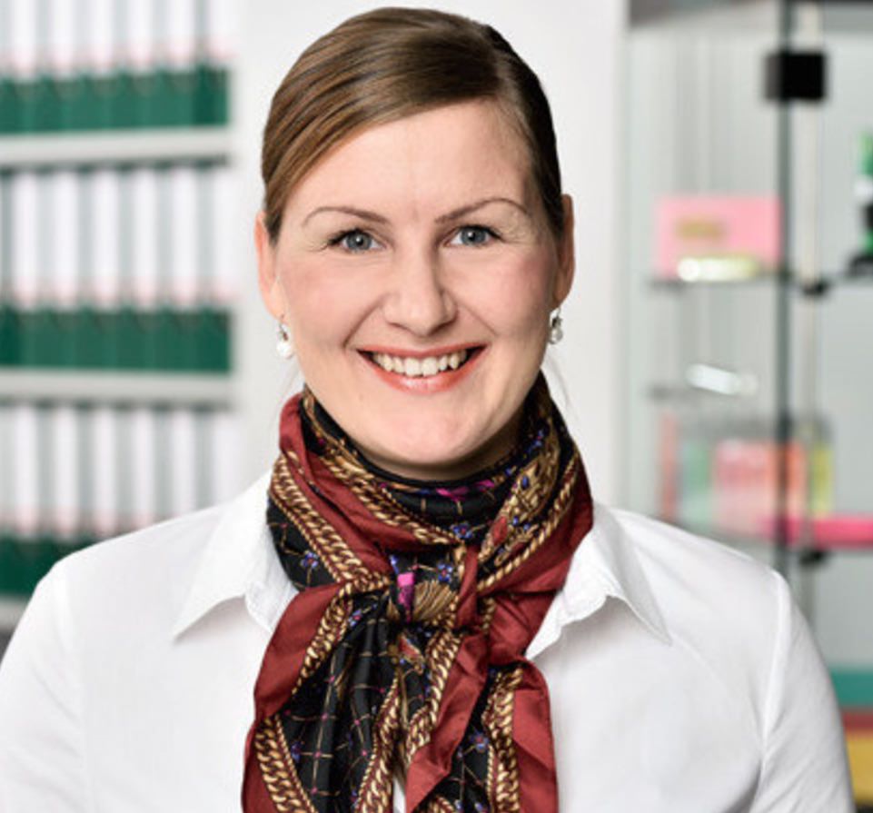 Frau Christina Sonntag mit braunem Haar, Perlentropfen-Ohrringe, weißer Bluse, rotes Tuch, Porträt vor Bücherregal