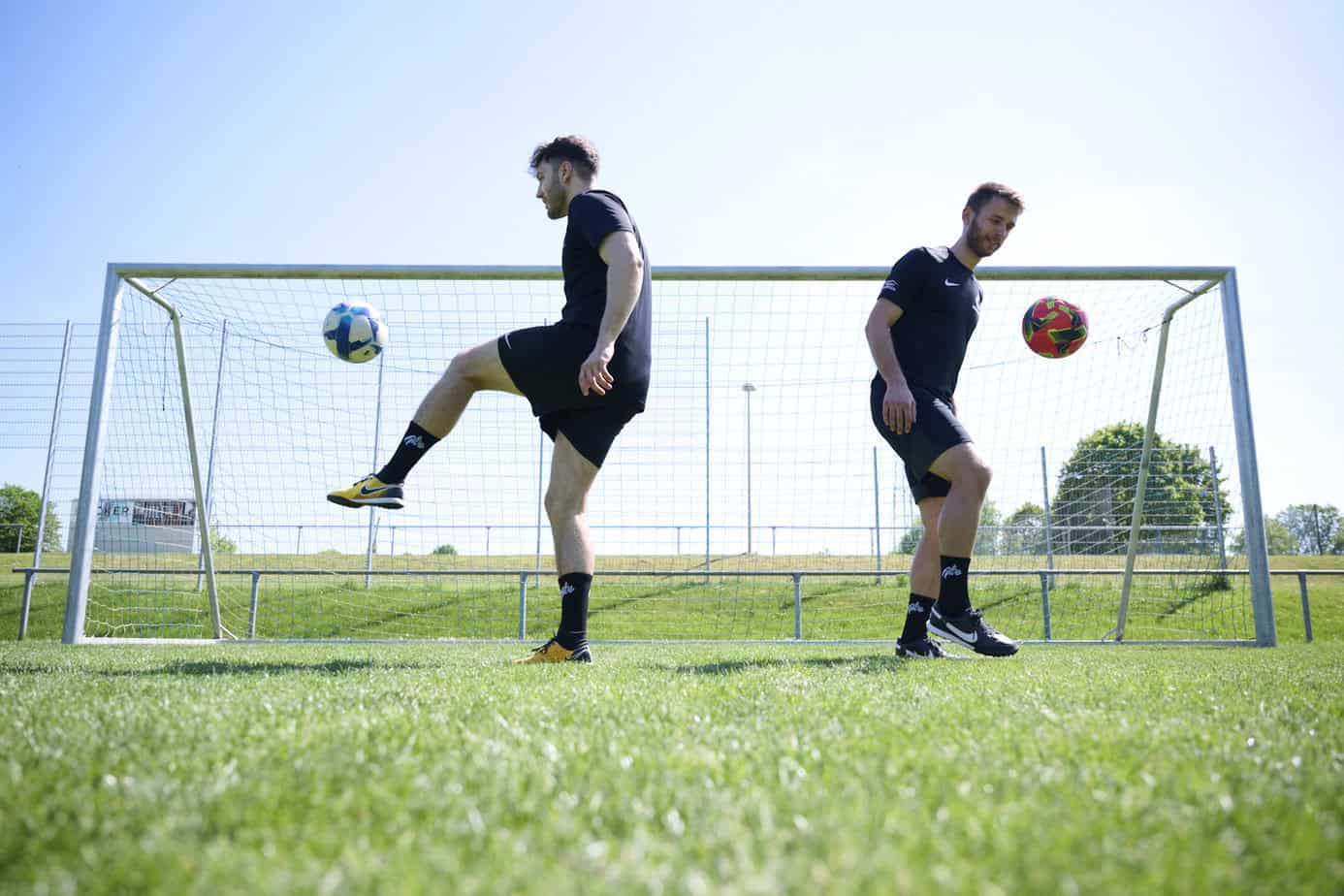 Zwei Fußballspieler trainieren mit Bällen vor einem Tor auf dem Platz
