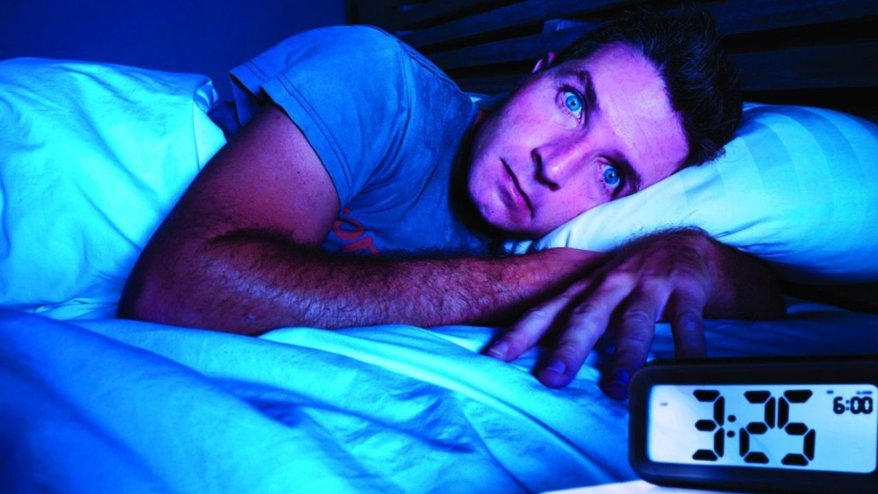 Mann nachts im Bett wach mit blaupurpurem Licht, besorgt, digitale Uhr zeigt 3:25 Uhr