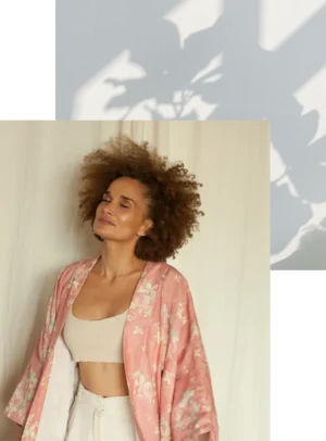 Frau mit lockigem Haar in rosa Blumenjacke und Crop Top vor heller Wand