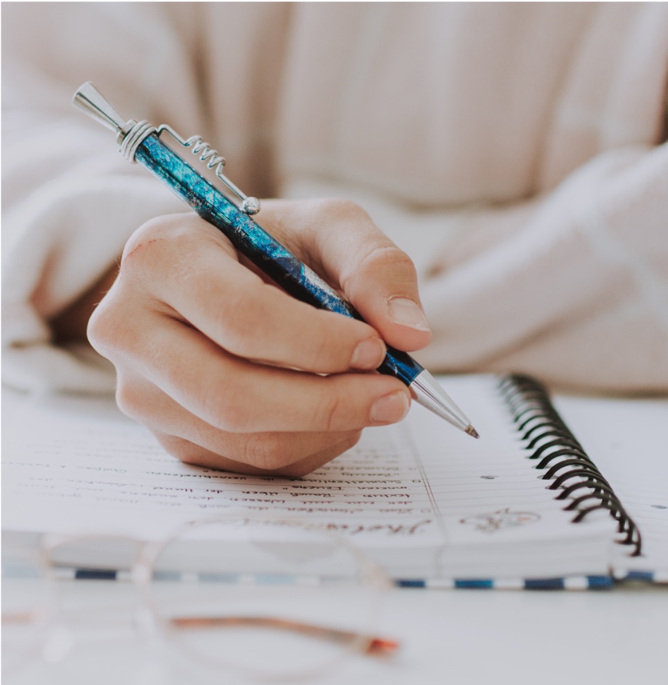 Hand schreibt mit blauem Stift in Notizbuch auf Sprachlernmaterialien