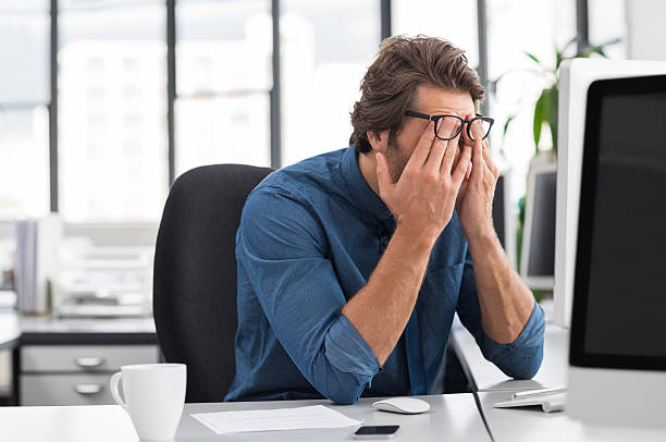 Mann mit Brille am Schreibtisch mit Computer wirkt überarbeitet und gestresst