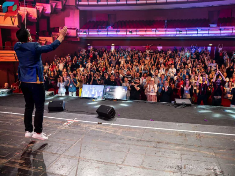 João Heep spricht vor großem Publikum in illuminiertem Auditorium, trägt blaues Blazer