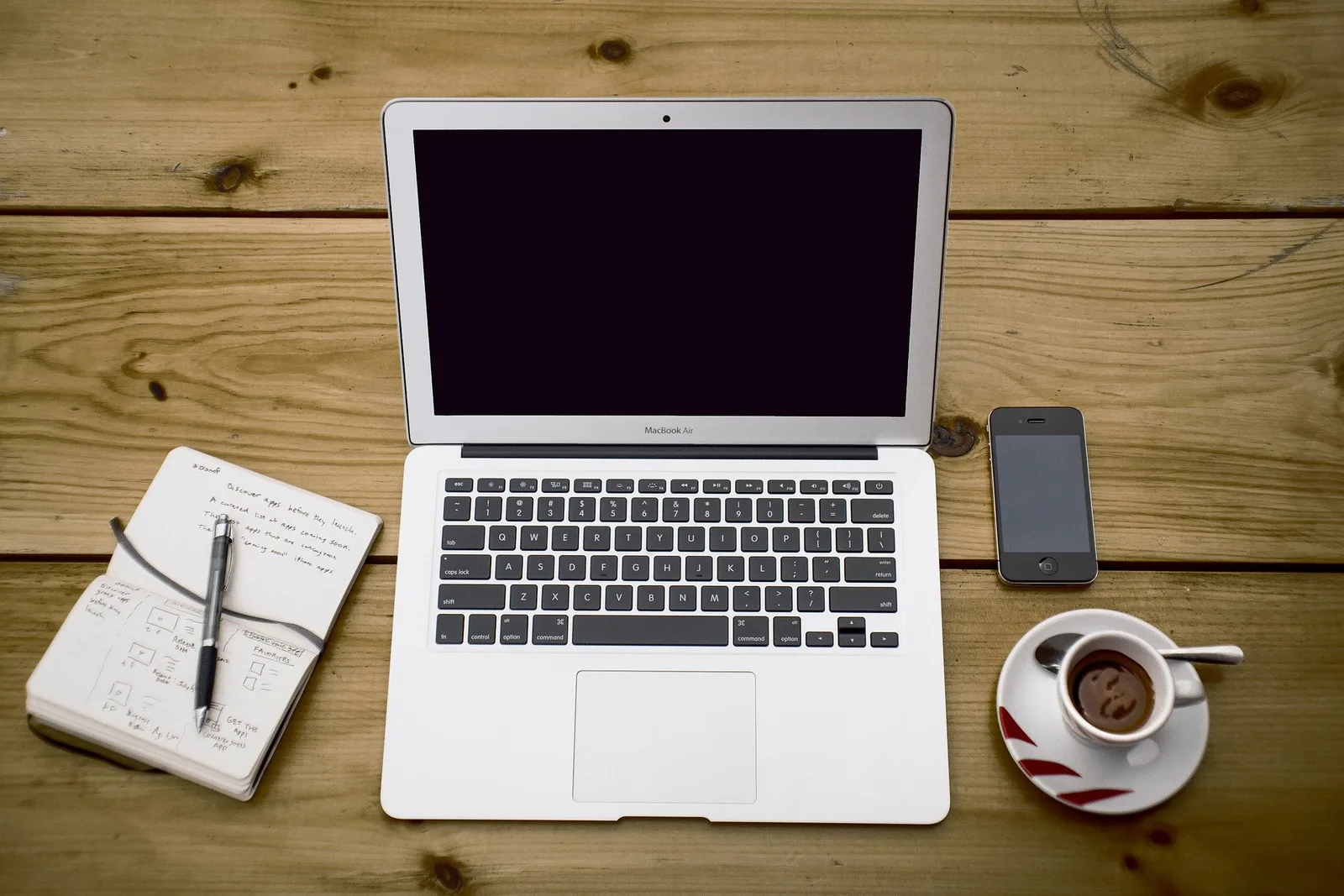 MacBook Air auf Holztisch mit Notizbuch, Smartphone und Kaffeetasse