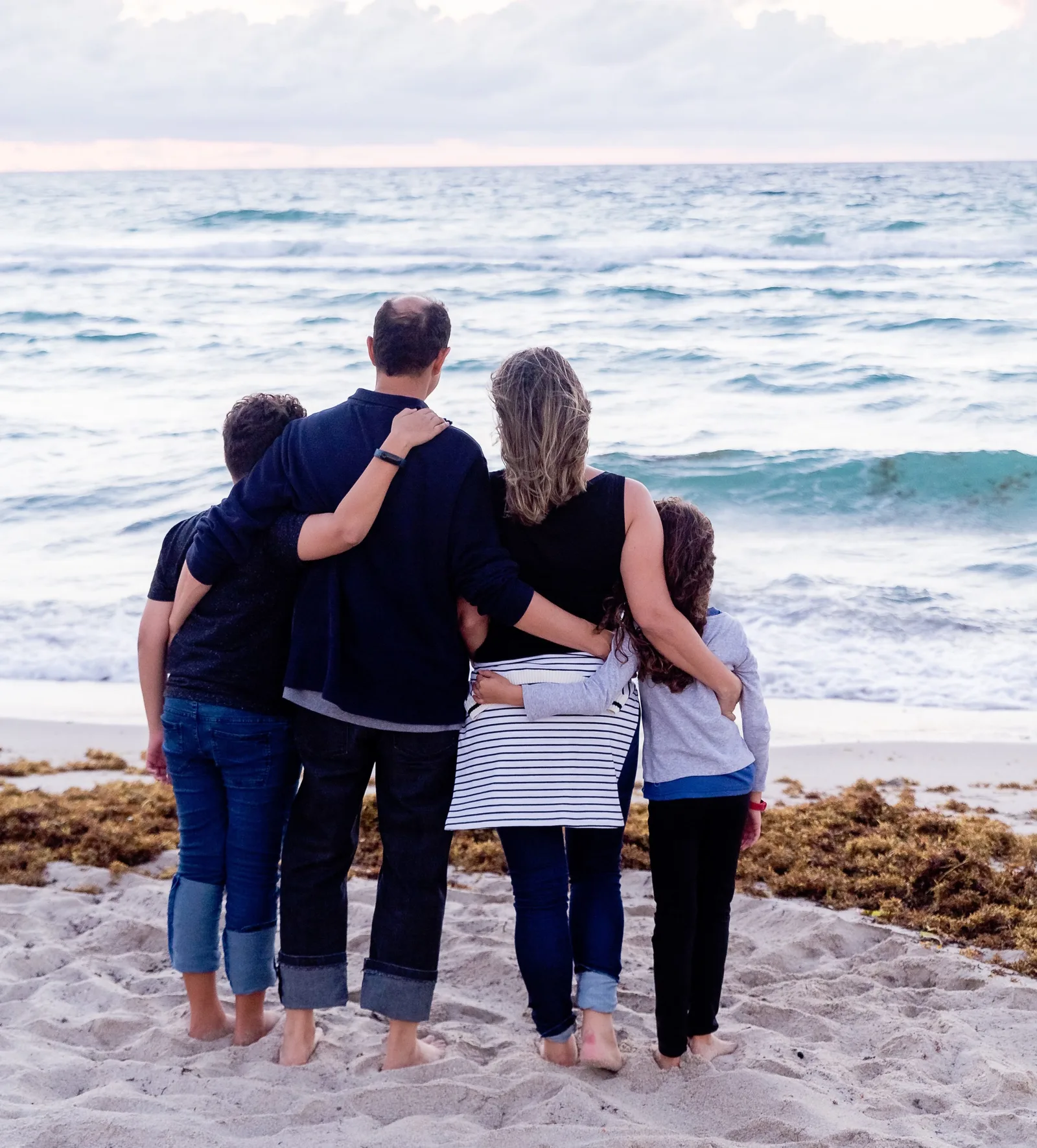 Familie mit vier Personen von hinten am Strand mit Blick auf das Meer