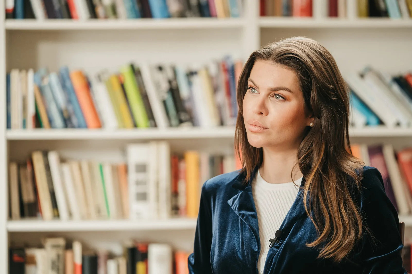 Frau in dunklem Blazer vor unscharfem Bücherregal, Porträt