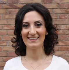Profilbild einer Frau mit dunklen Haaren vor Backsteinwand