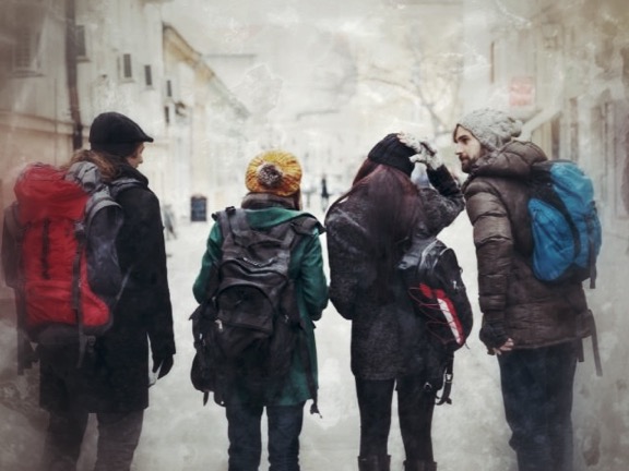 Gruppe von fünf Personen mit Rucksäcken von hinten in historischer Gasse, eine Person zeigt mit Handy