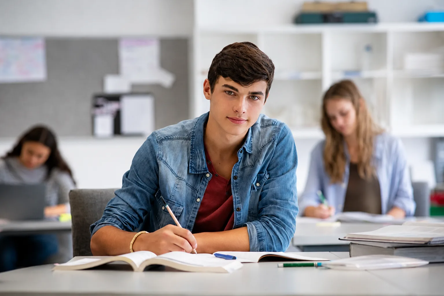 Startklar! – Mentale Stärke für Studium & Berufseinstieg 5 Student konzentriert am Schreibtisch mit Buch und Notizen, weitere Schüler im Hintergrund