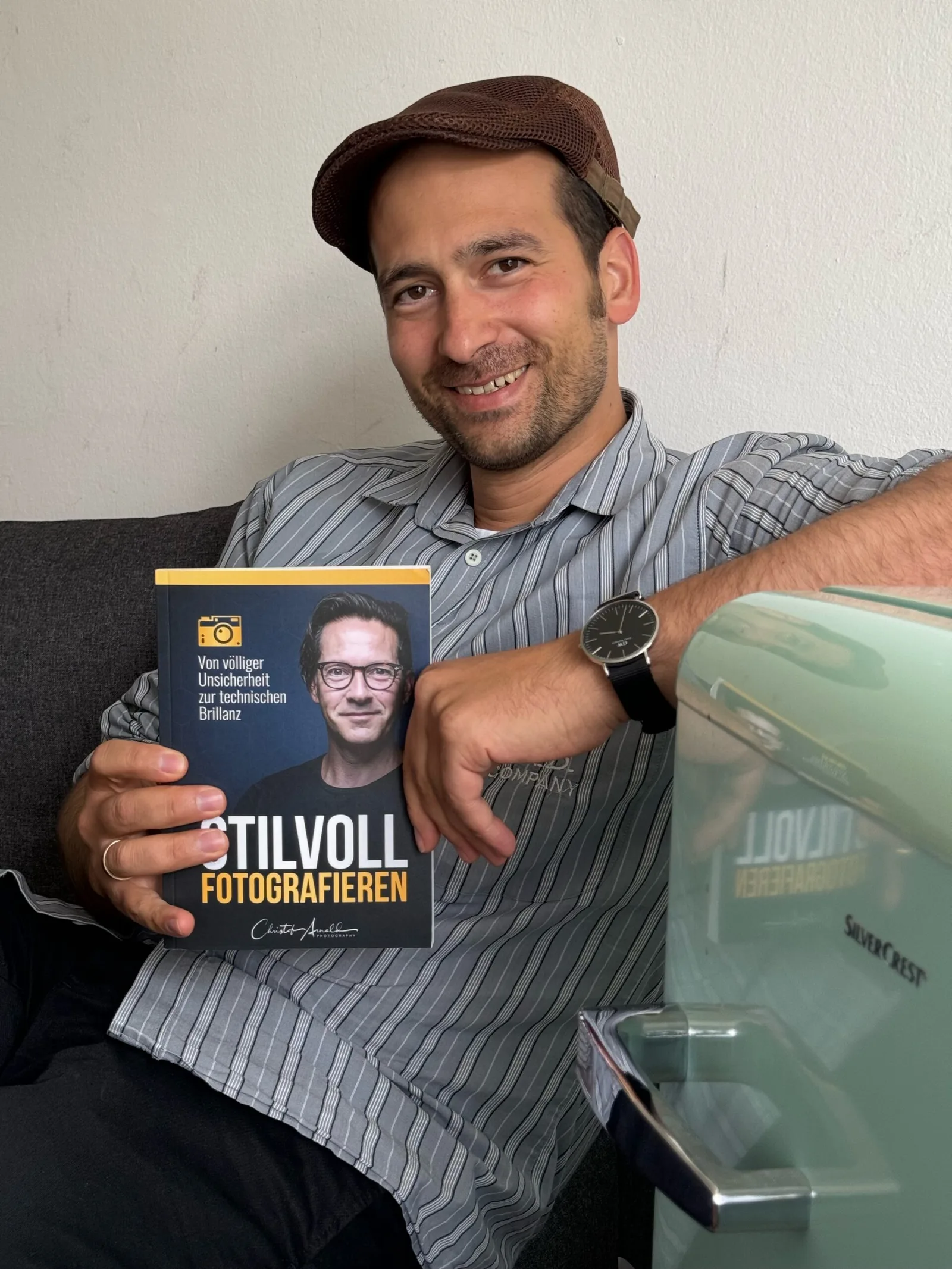 Mann in gestreiftem Hemd und braunem Cap hält das Buch Stilvoll Fotografieren