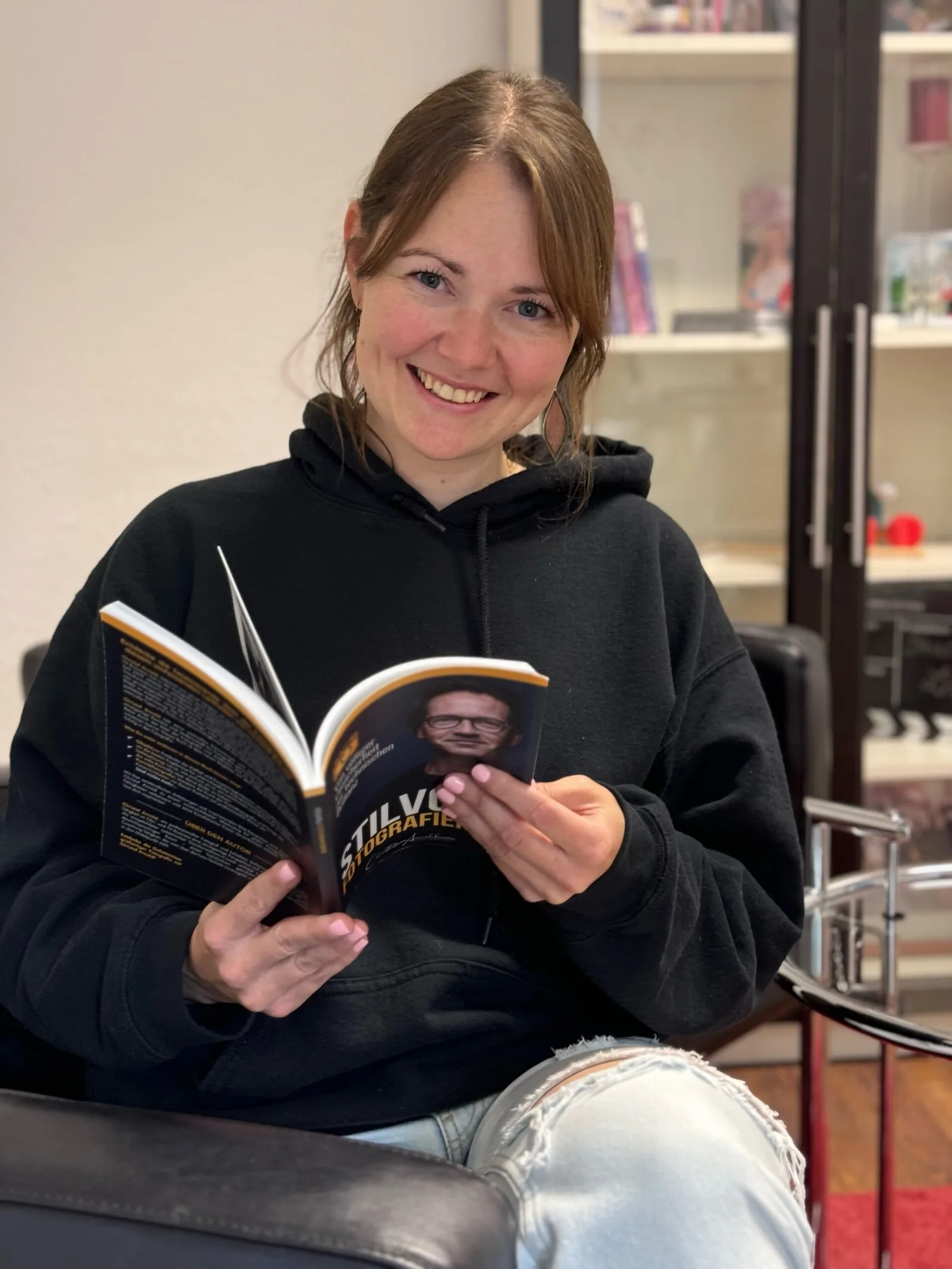 Junge Frau in schwarzem Hoodie mit offenen Buchseiten des Werks Stilvoll Fotografieren