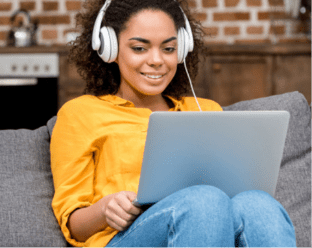 Frau mit Kopfhörern sitzt auf Sofa mit Laptop und arbeitet am Kurs