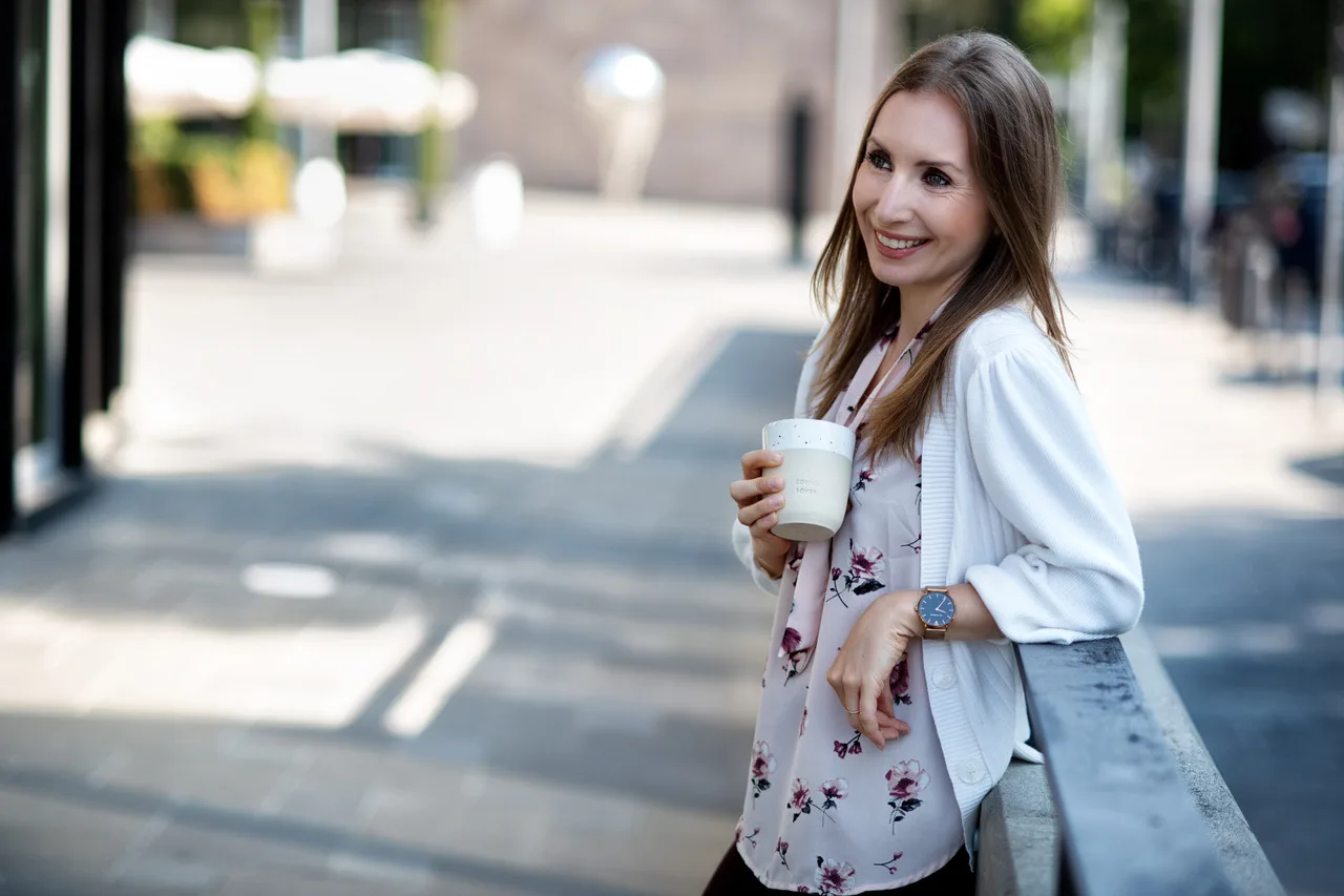 Porträt einer Frau mit Kaffeebecher in urbaner Umgebung, lächelnd