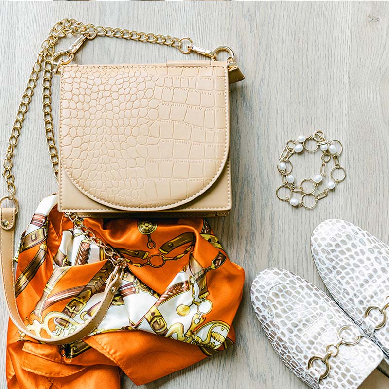 Styling-Kombination mit beigefarbener Handtasche, orangefarbenes Halstuch und weißen Schuhen auf Holzuntergrund