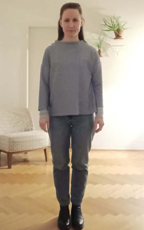 Frau in grauem Pullover und dunkler Jeans, stehend im Wohnzimmer, Vorher-Foto