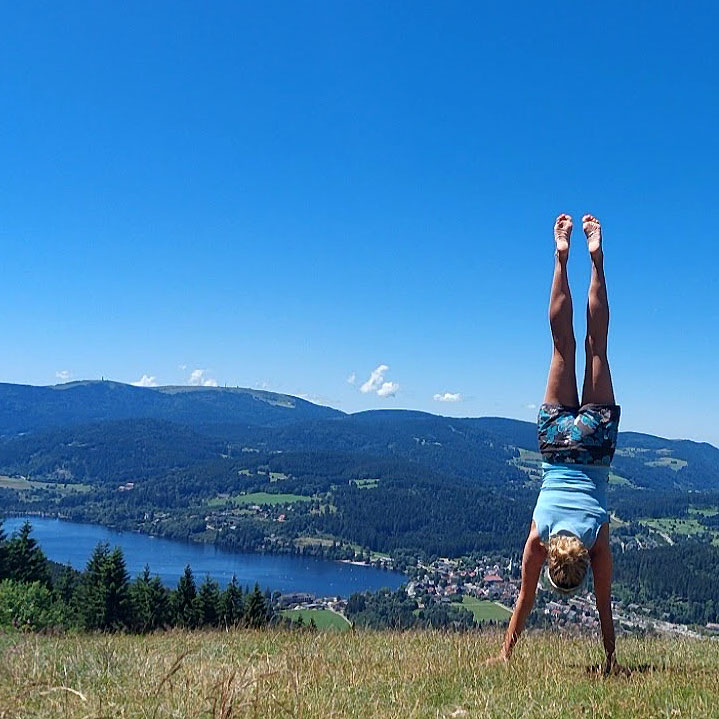 Suchtakademie Online – Videokurs gegen Sucht von Liv Wach 4 Person macht Kopfstand in bergiger Landschaft mit See, Yoga und Achtsamkeit