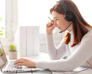 Frau mit Headset und Laptop sitzt an weißem Schreibtisch mit Pflanze