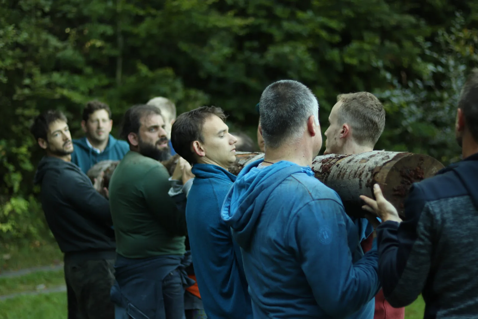 Gruppe von sieben Männern in blauer Sportkleidung um Baumstamm versammelt im Wald