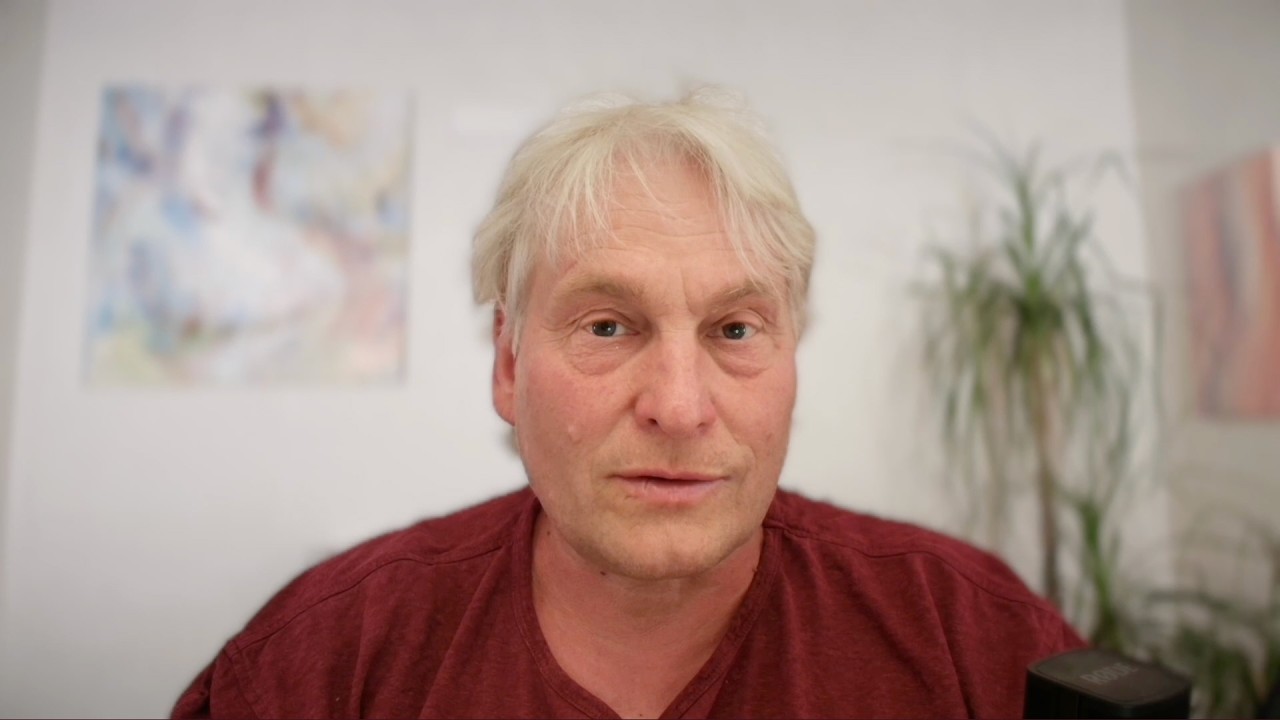 Porträt eines älteren Mannes mit weißem Haar in dunkelrotem Shirt vor unscharfem Hintergrund