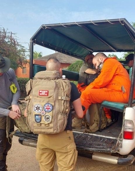 Sanitäter in orangener Schutzausrüstung mit taktischem Rucksack in Fahrzeug