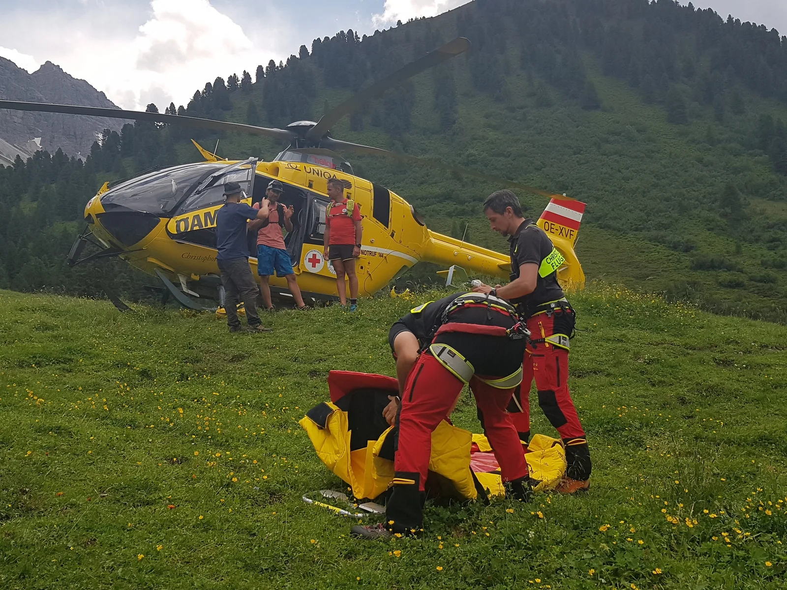 Gelber Rettungshubschrauber mit Sanitätern und Patienten auf Bergwiese
