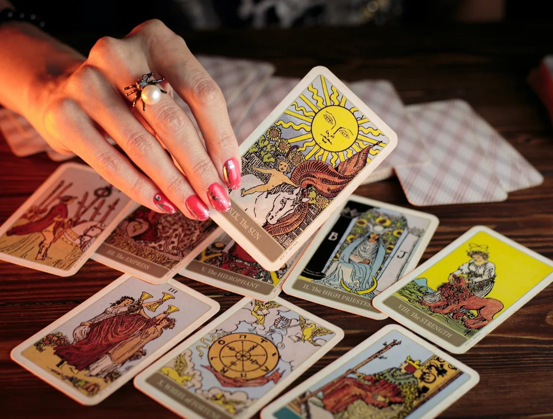Weibliche Hand mit roten Nägeln beim Auslegen von Tarot-Karten, The Sun Karte prominent, mehrere Karten sichtbar