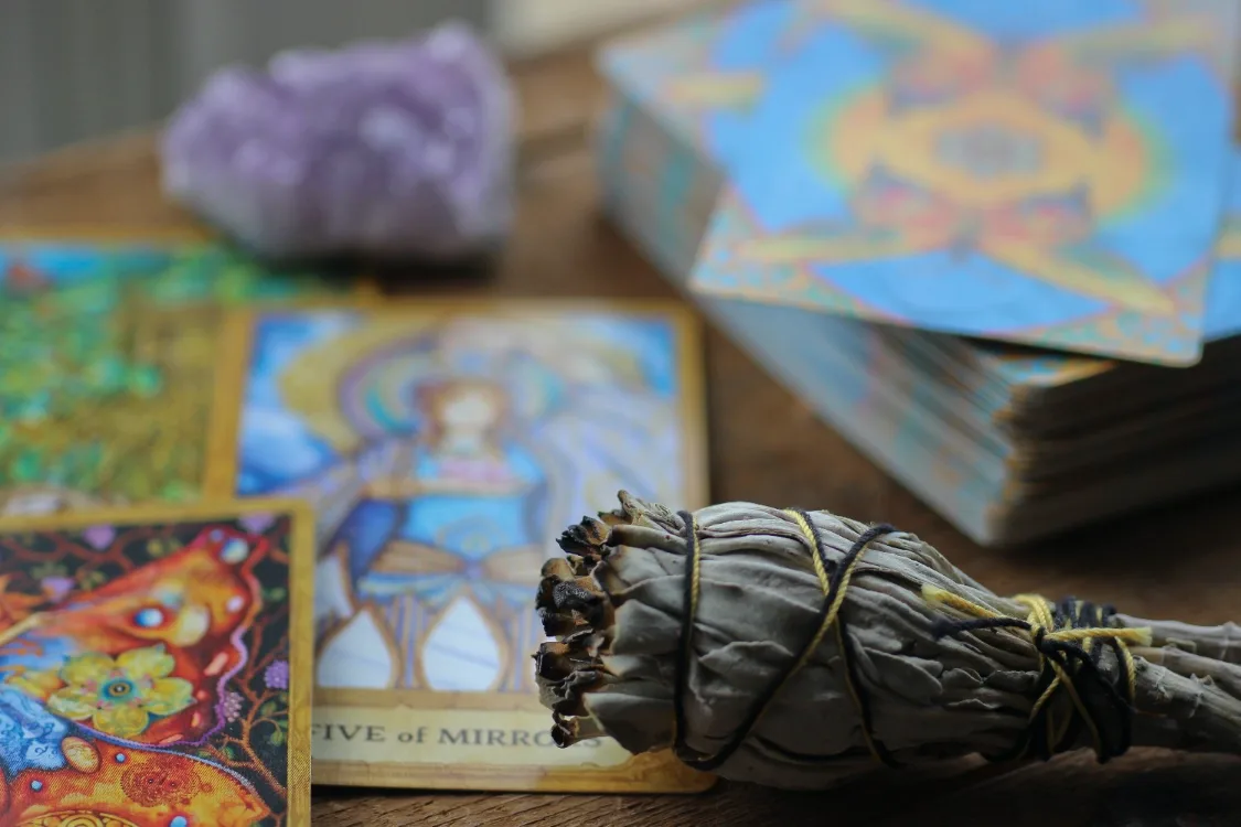 Tarot-Karten und Zubehör auf Holzoberfläche, Räucherbündel, Amethyst-Kristall und aufgeschlagene Tarot-Bücher