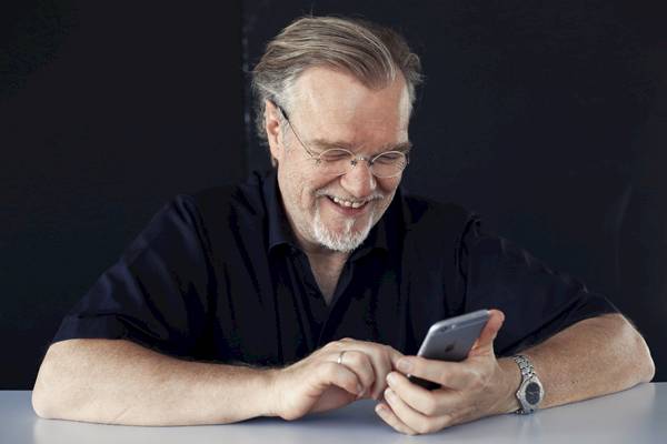 Mann mit Brille in schwarzem Hemd hält Smartphone in den Händen und blickt darauf