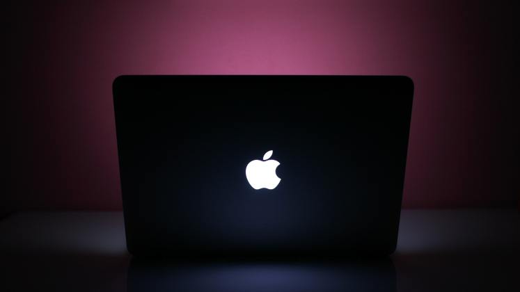 Apple MacBook mit leuchtender Logo auf dunklem violettem Hintergrund