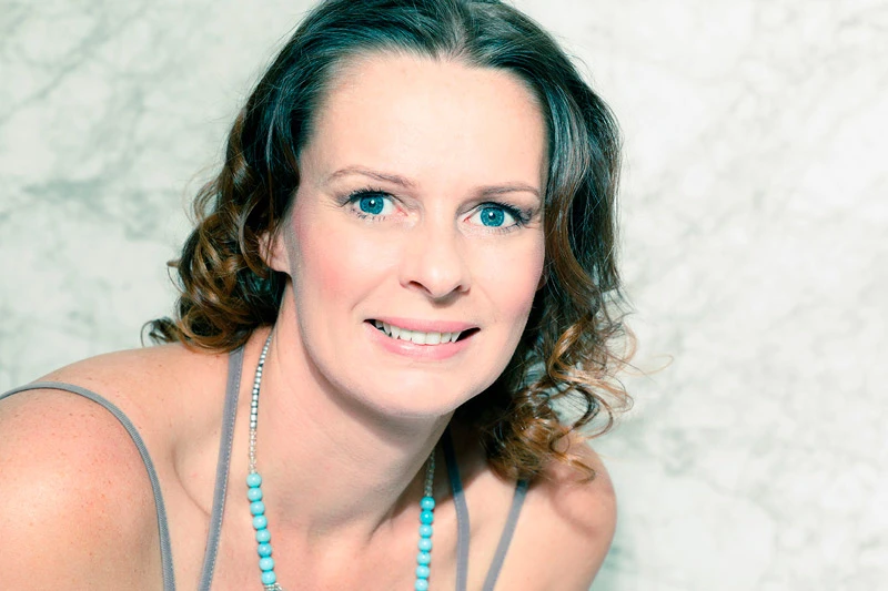 Porträt einer Frau mit braunen lockigen Haaren und grauem Top, lächelnd