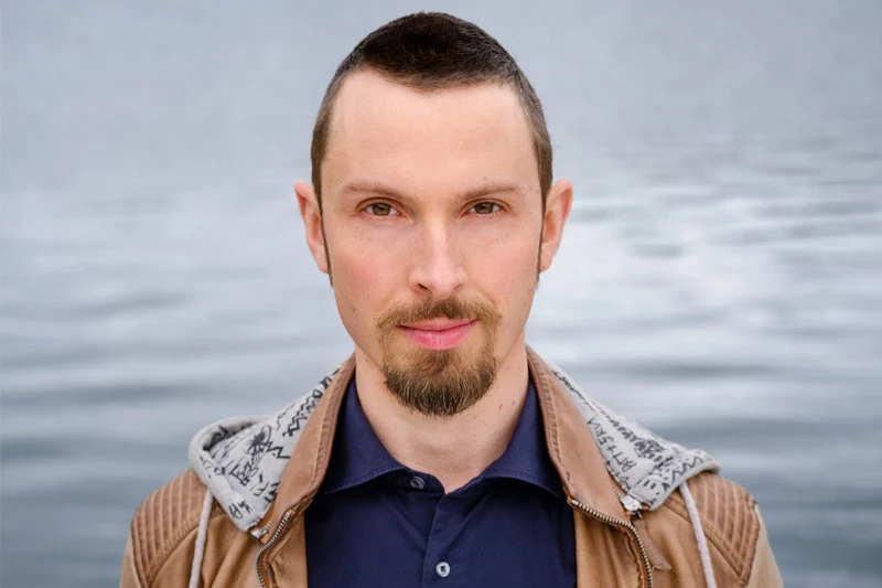 Porträt von Tobias Frank, Mann mit Bart vor Wasser-Hintergrund