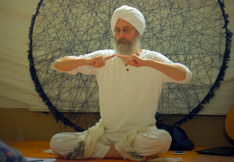 Mann mit weißem Turban und Bart sitzt meditierend vor blauem Mandala-Kreis