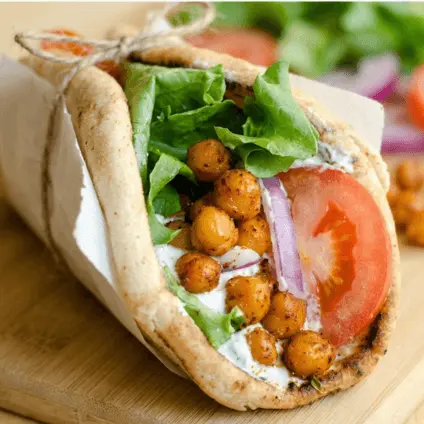 Vollkorn-Wrap gefüllt mit gerösteten Kichererbsen, Salat und Tomaten auf Holzbrett
