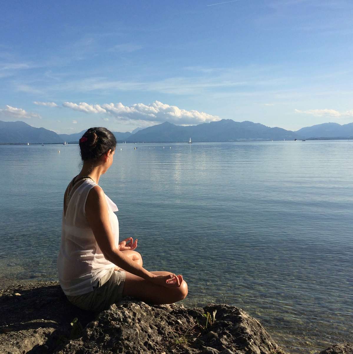 Yoga-Trainerin sitzt meditierend am Seeufer mit Bergblick