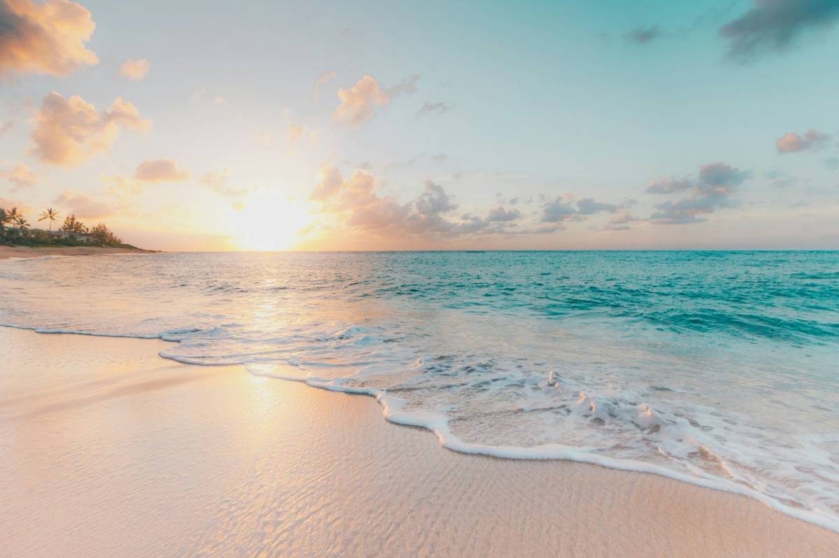 Tropischer Strand bei Sonnenuntergang mit feinen Wellen und Palmen am Horizont